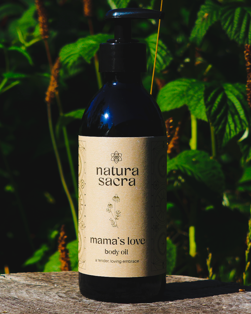 Natura Sacra Mama's Love body oil bottle with a natural label against a green leafy background.